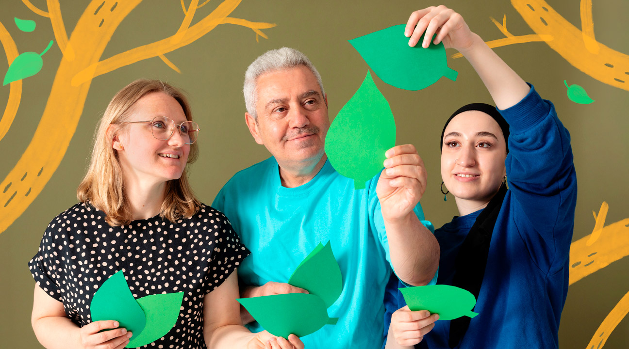 Three people arrange green tree leaves cut out of paper into the air. Drawn tree branches have been added to the picture.