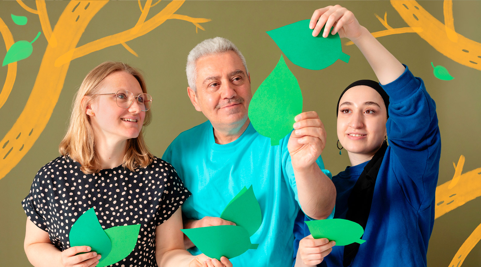 Kolme henkilöä asettelee ilmaan paperista leikattuja vihreitä puun lehtiä. Kuvaan on lisätty puun oksia piirroskuvituksen muodossa.