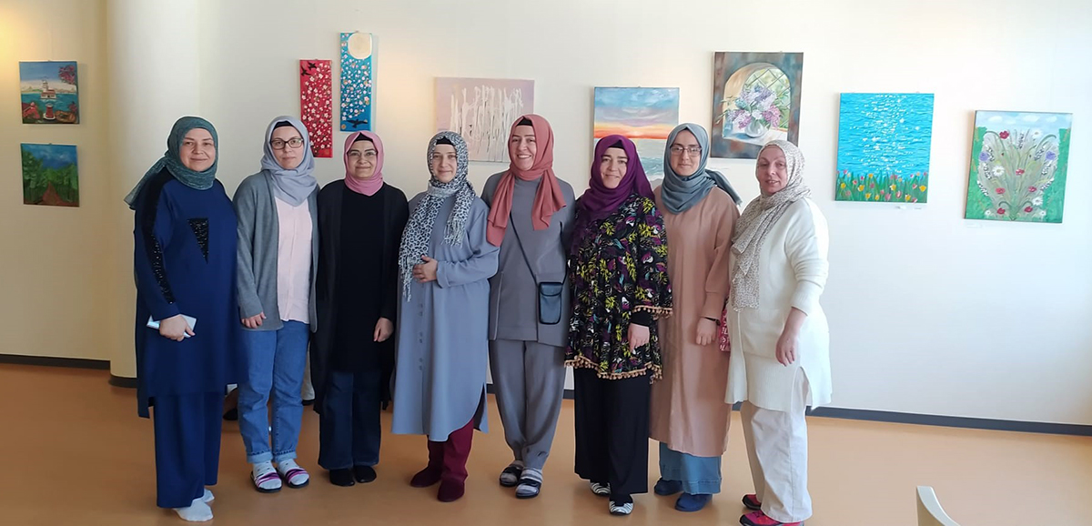 Course participants and the teacher in a joint photo in front of artworks mounted on the wall.